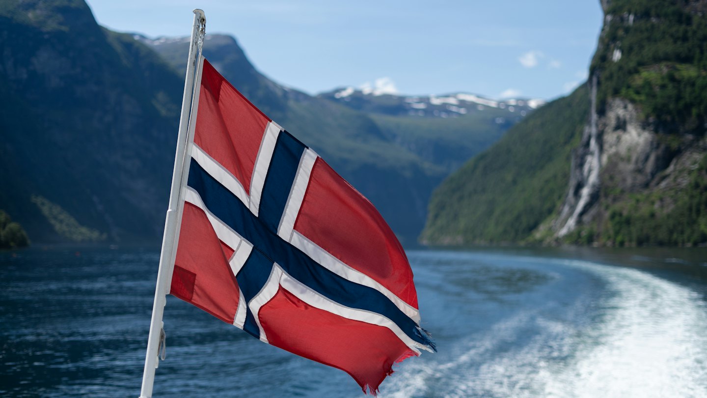 Norweska flaga na tle malowniczego fiordu z górami i wodospadem.
